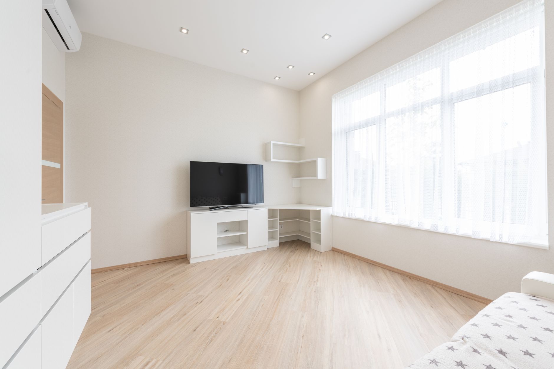 壁の高い位置にエアコンが付いた明るい部屋。エアコンは外の空気から熱を集めて室内に運ぶヒートポンプ方式