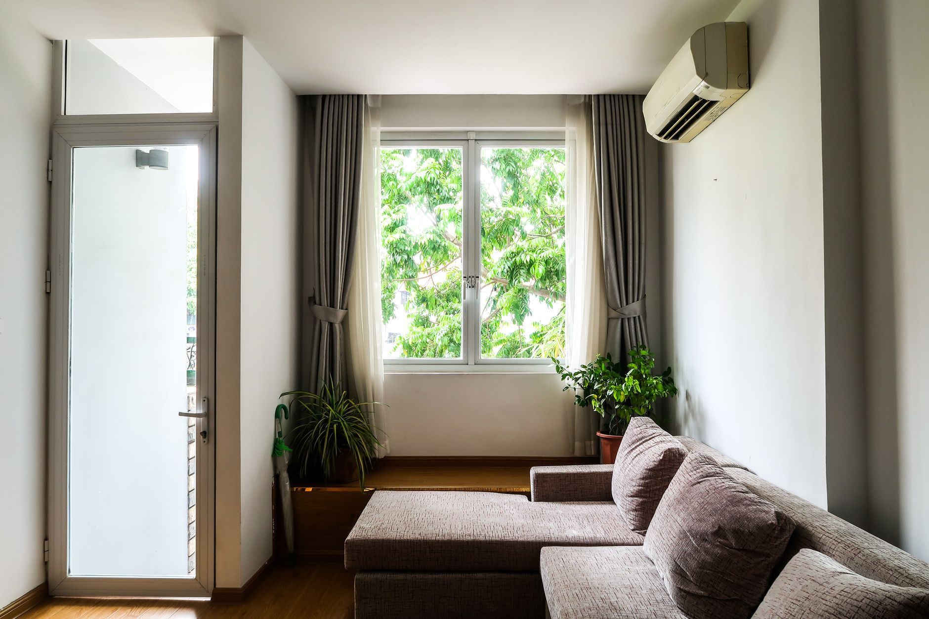 窓とエアコンがある明るい部屋。スポットクーラーは室外機にあたる部分を本体に抱えているため排熱処理が必要になる