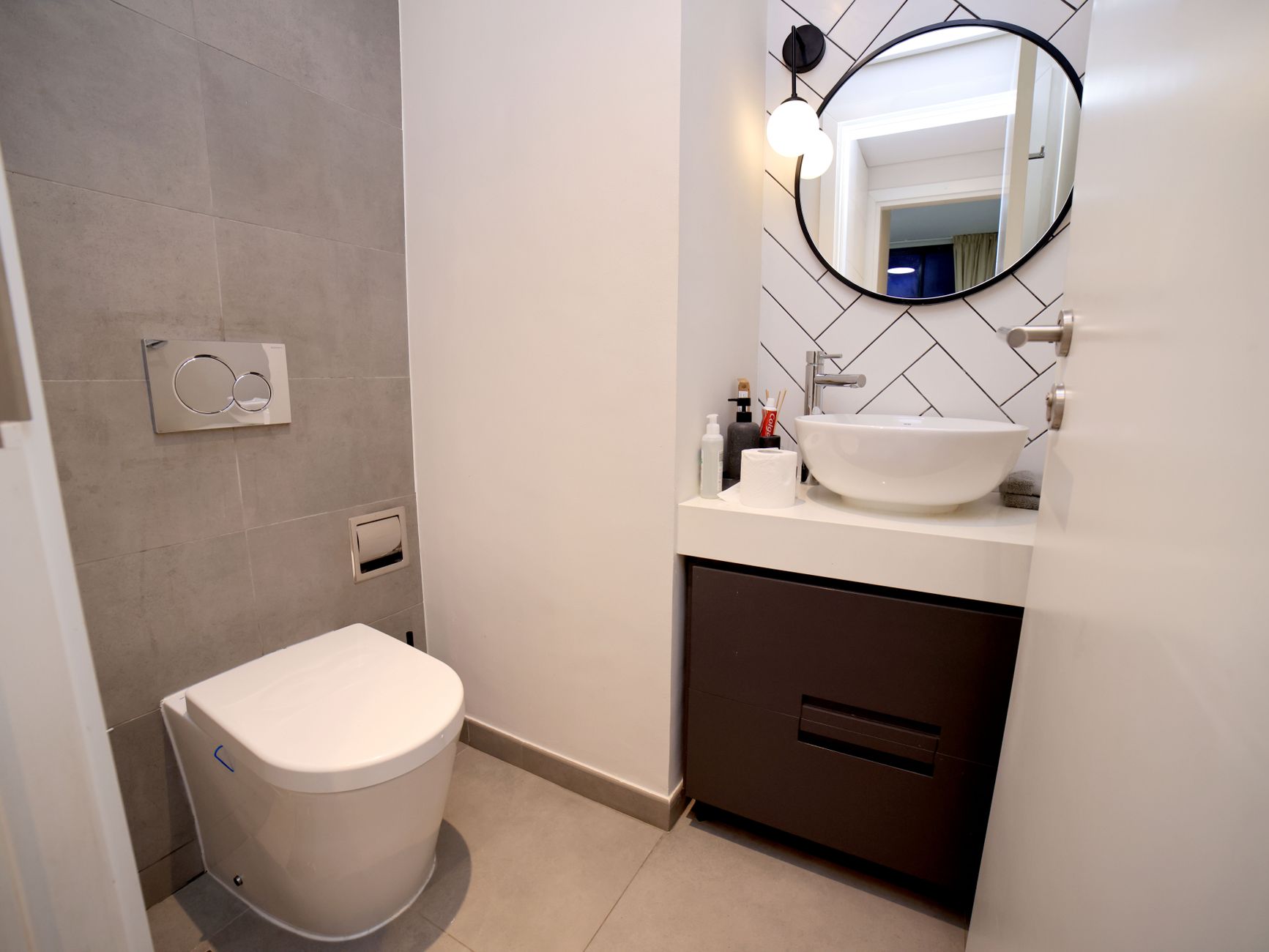 便器と手洗いカウンターが向かい合う狭いトイレ。滞在時間が短いなら温風、底冷えが続くなら無風タイプが向く