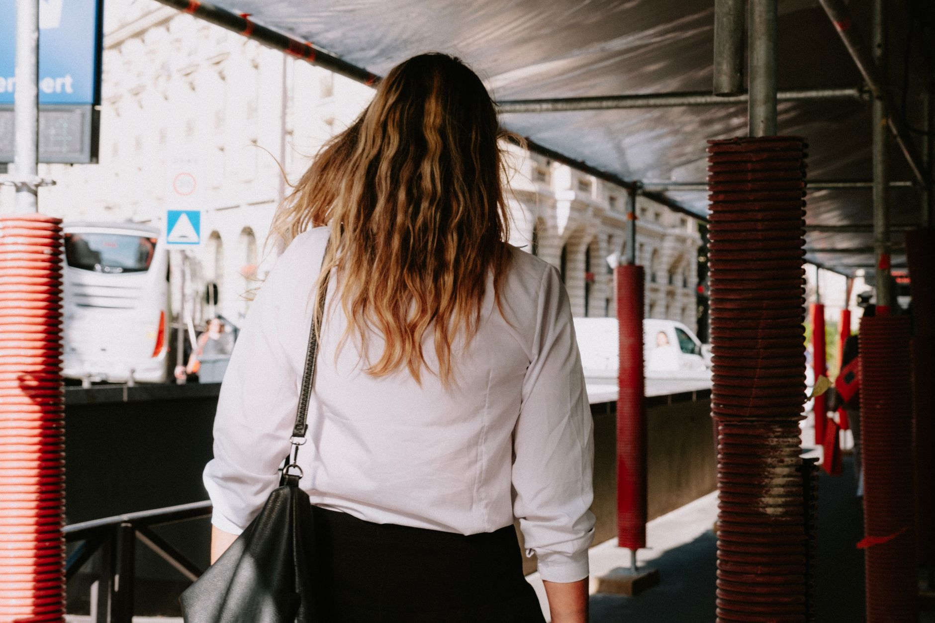 かばんを提げた人が、日中の街路を前を向いて歩いていくところ。
