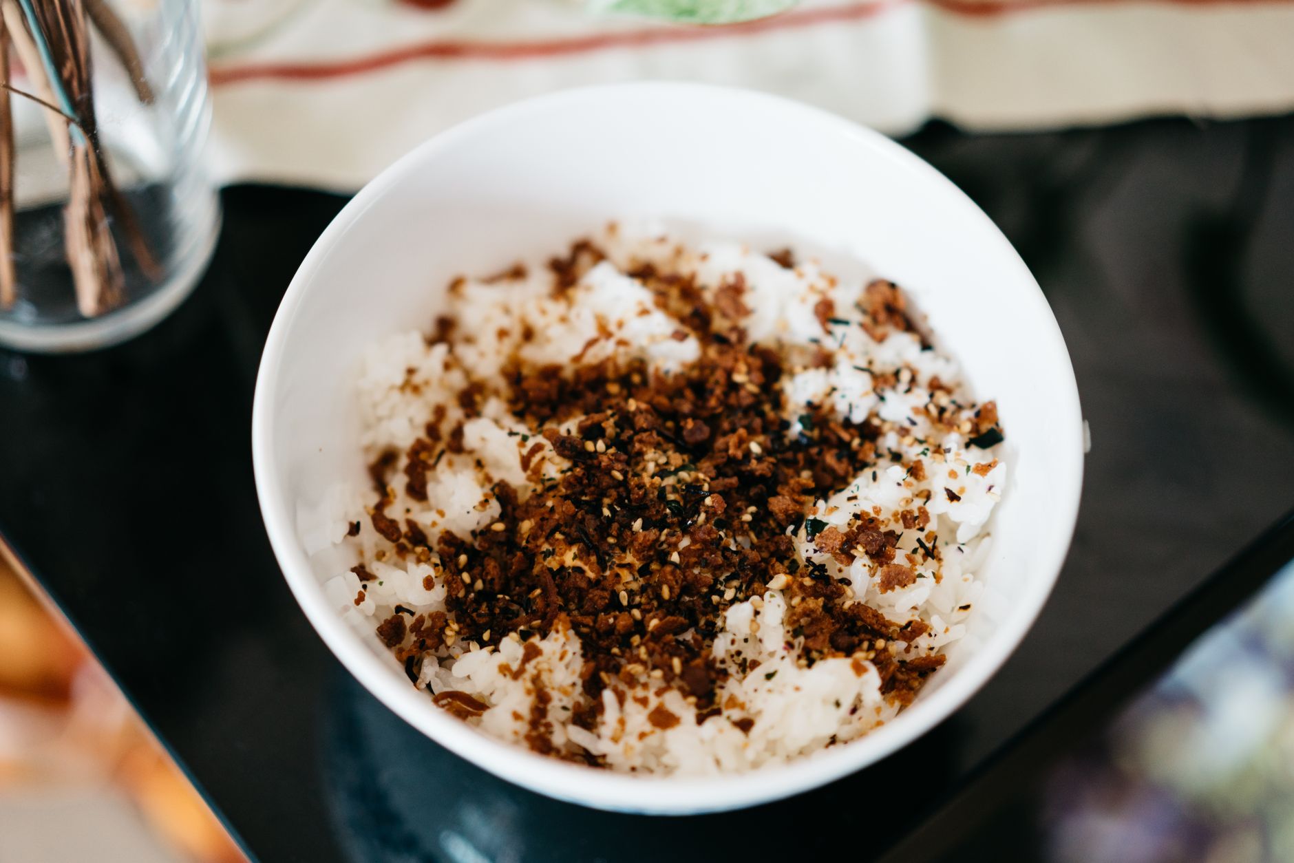 食卓に置かれた白い茶わんに、ふりかけをかけたごはんが盛られている。