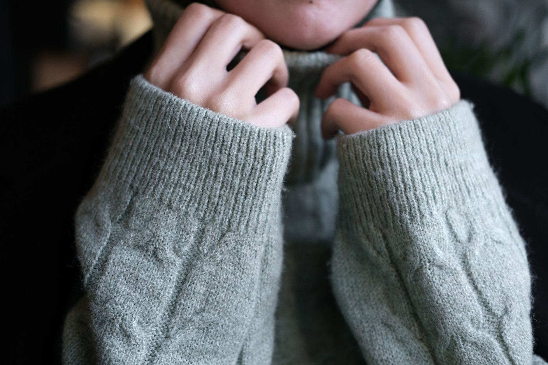 厚手のニットの袖口から指先だけを出し、襟元を引き上げている手元。
