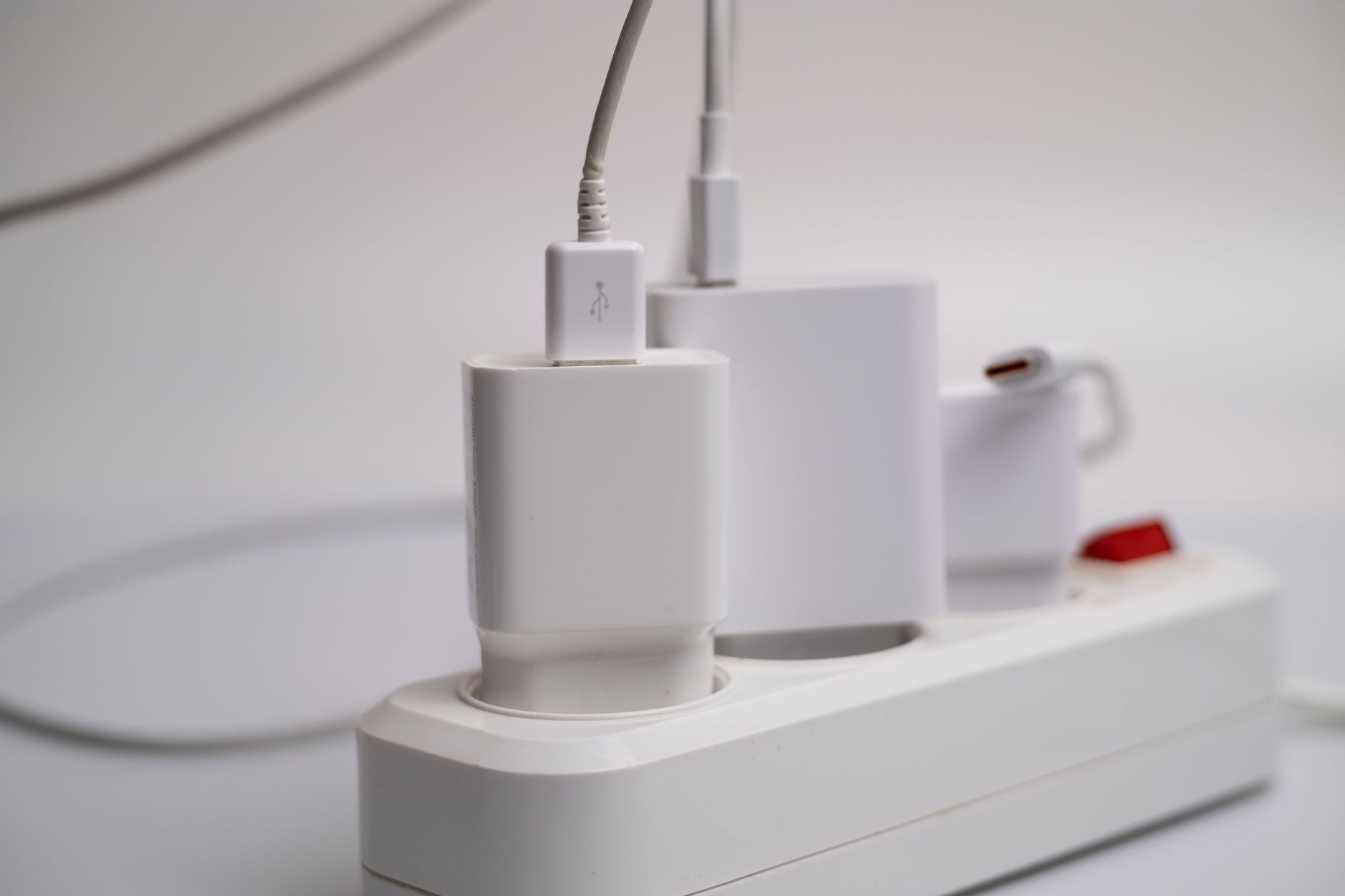 電源タップに挿さった白い充電器と、そこから伸びるケーブル。室内の机まわり。