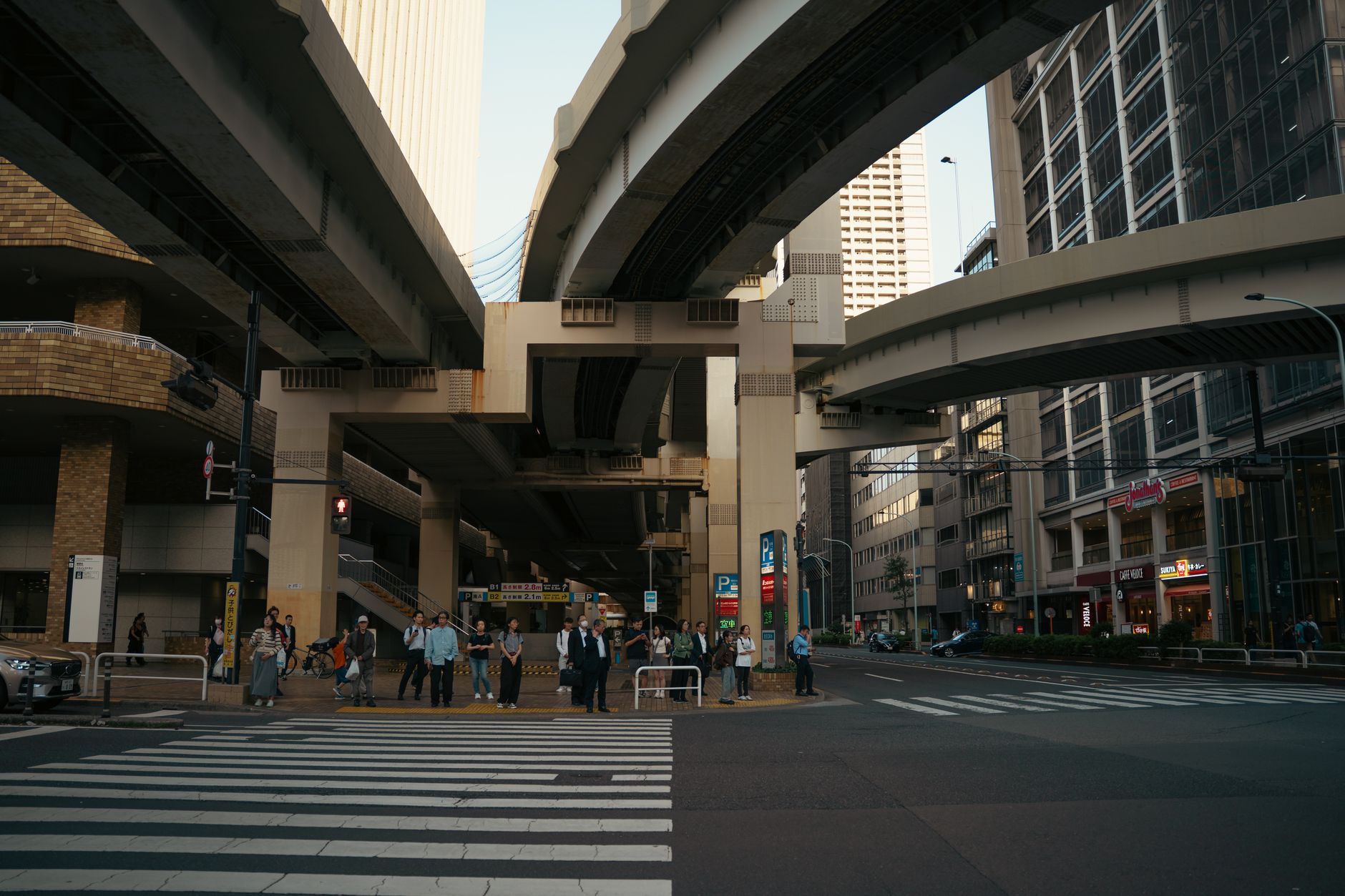 高架下の交差点で、横断歩道の信号が変わるのを待っている人たちの列。