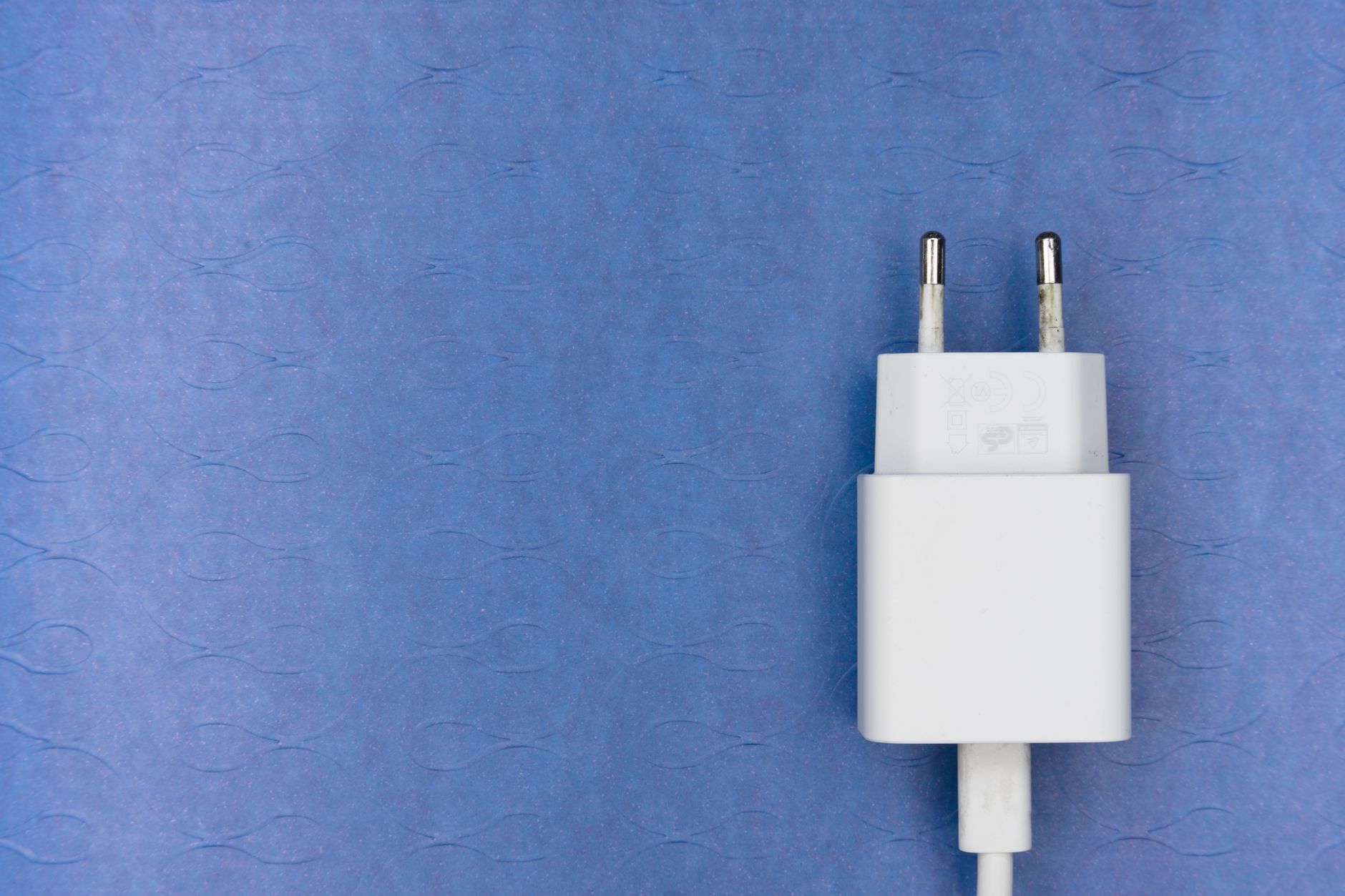 青い布地の上に置かれた、コードのついた白い充電アダプターのプラグ部分。