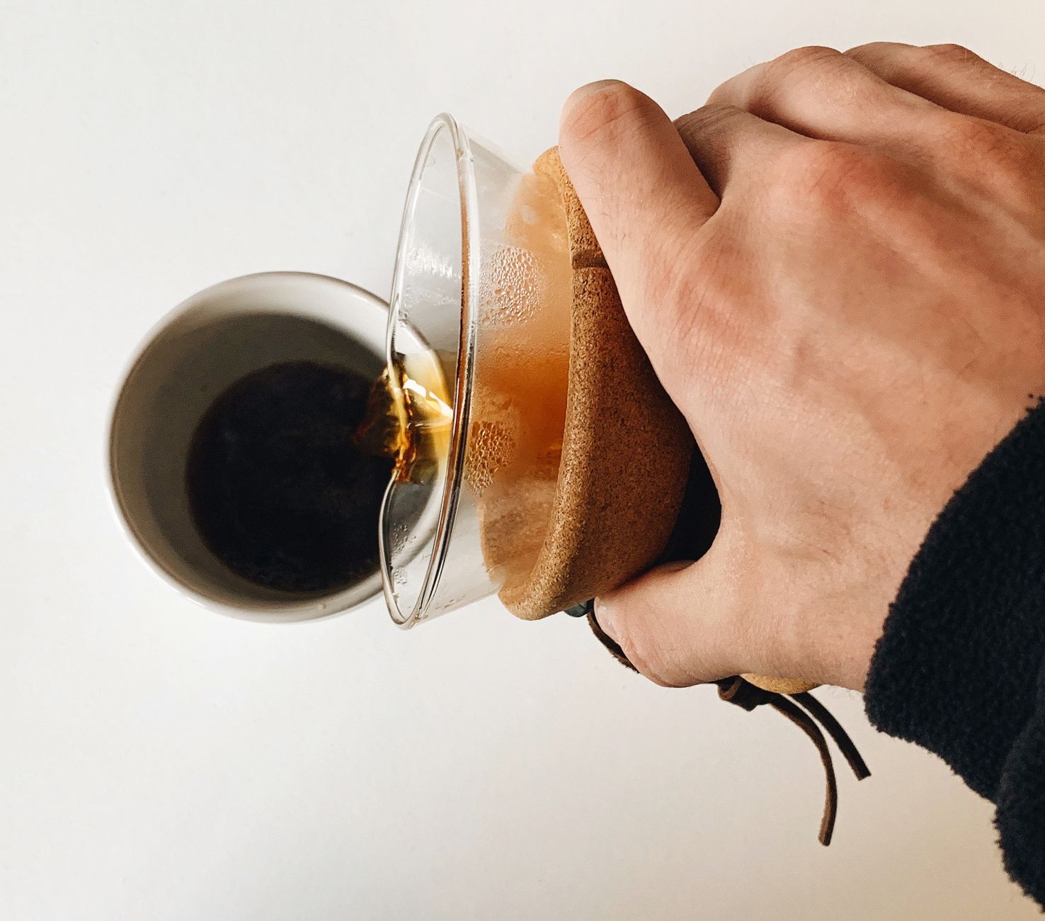 白い机の上で、ガラスの器から湯気の立つコーヒーをマグに注いでいる。