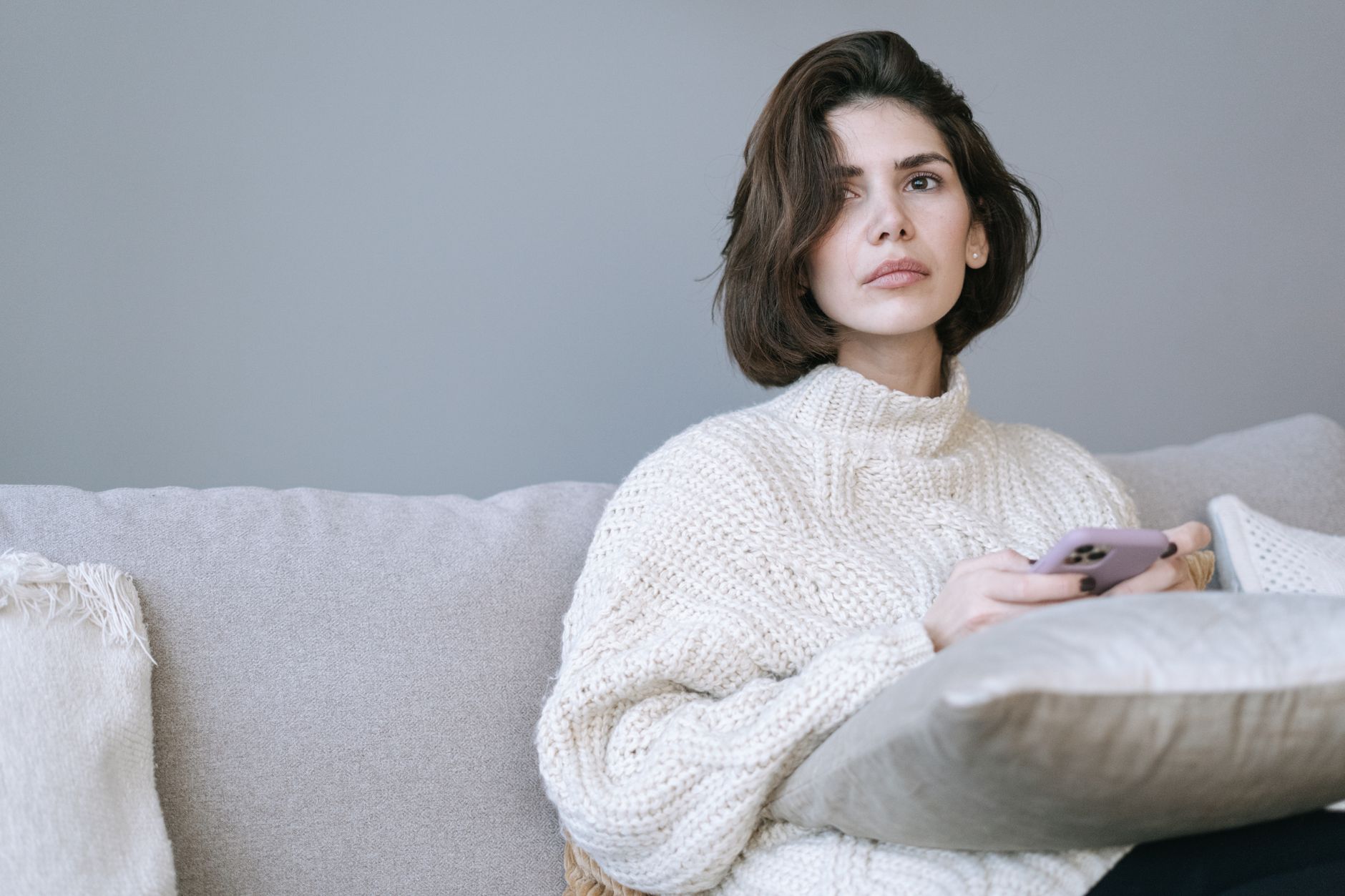 ソファに腰かけ、スマートフォンを手にしたまま考えごとをしている人。