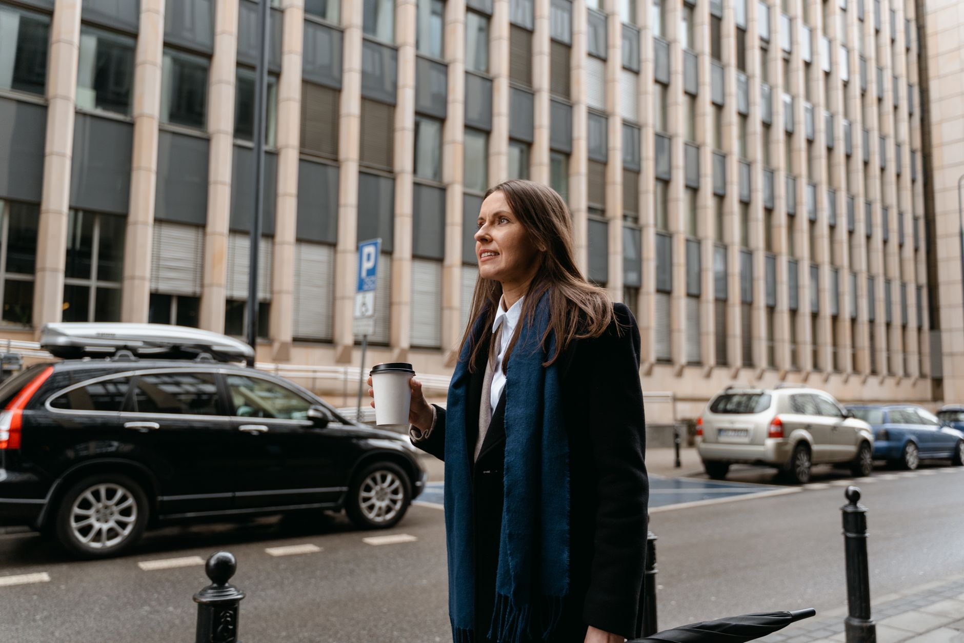 オフィス街の歩道で、紙コップを手に立ち止まっている外出中の女性。
