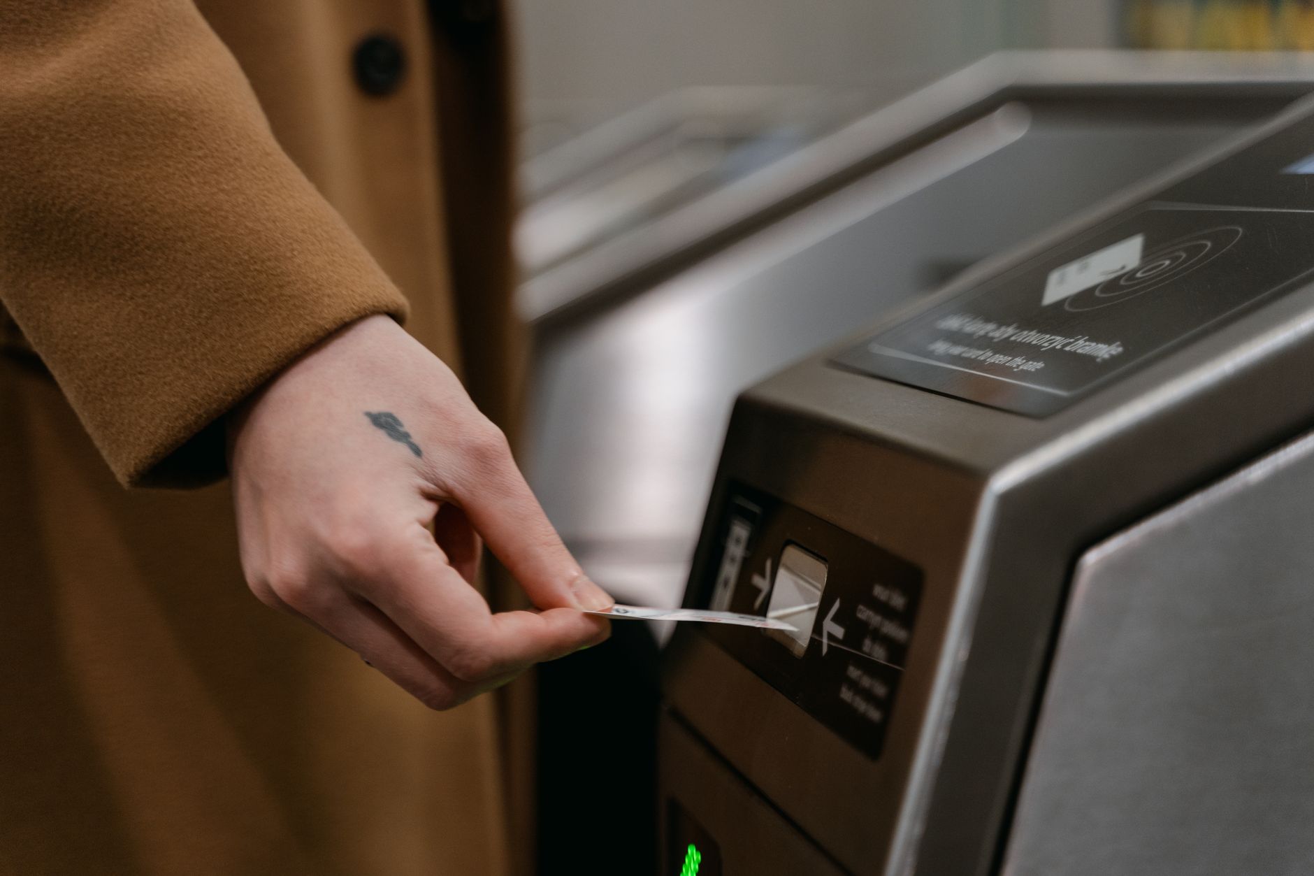 駅の改札機の投入口へ、切符を差し入れようとしているコートの人の手元。