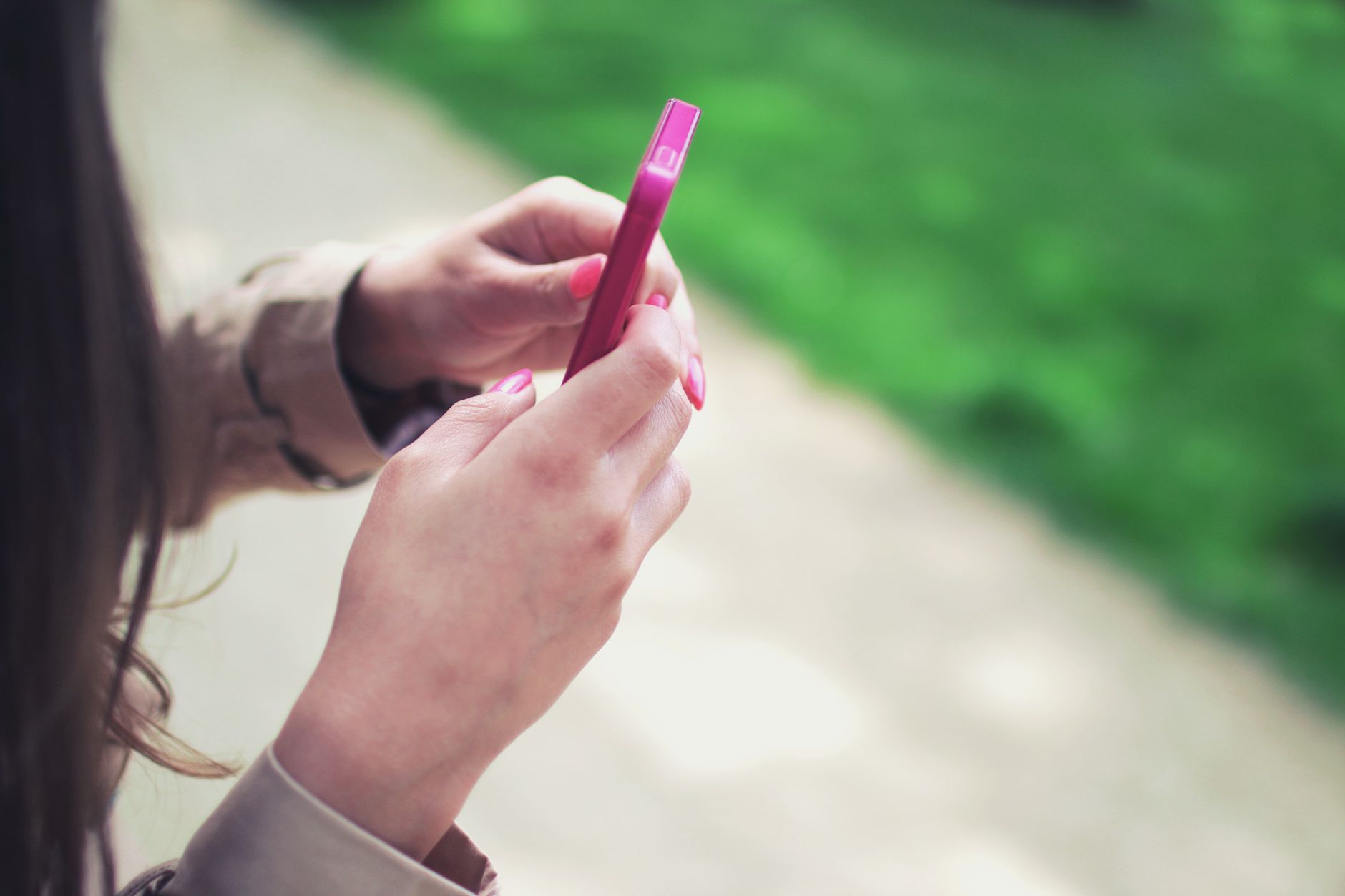屋外で、片手に持った小型のスマートフォンの画面を見ている人の手元。
