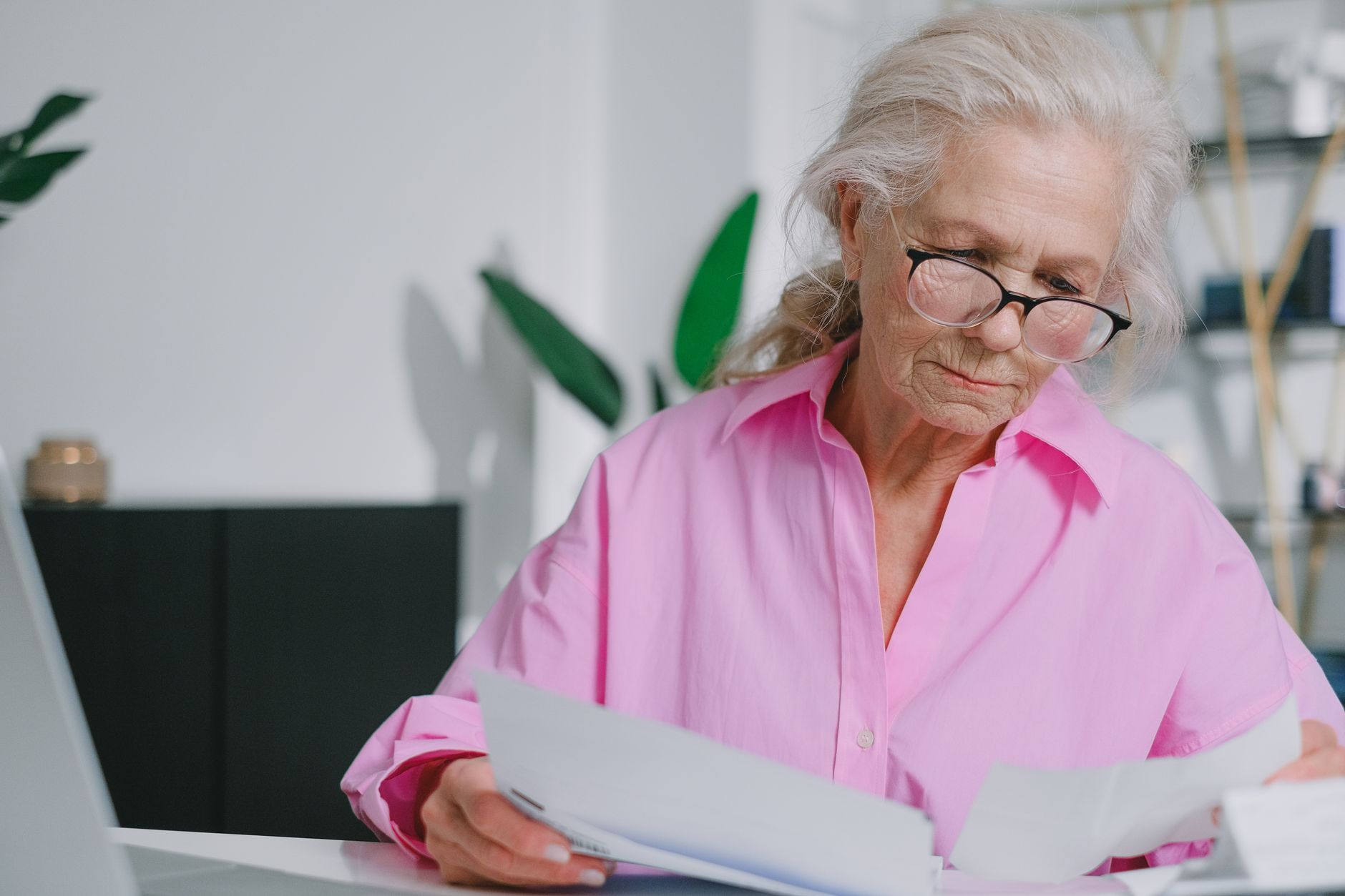 机に広げた書類に目を落とす人。眼鏡をかけて細かな表示を確かめている。