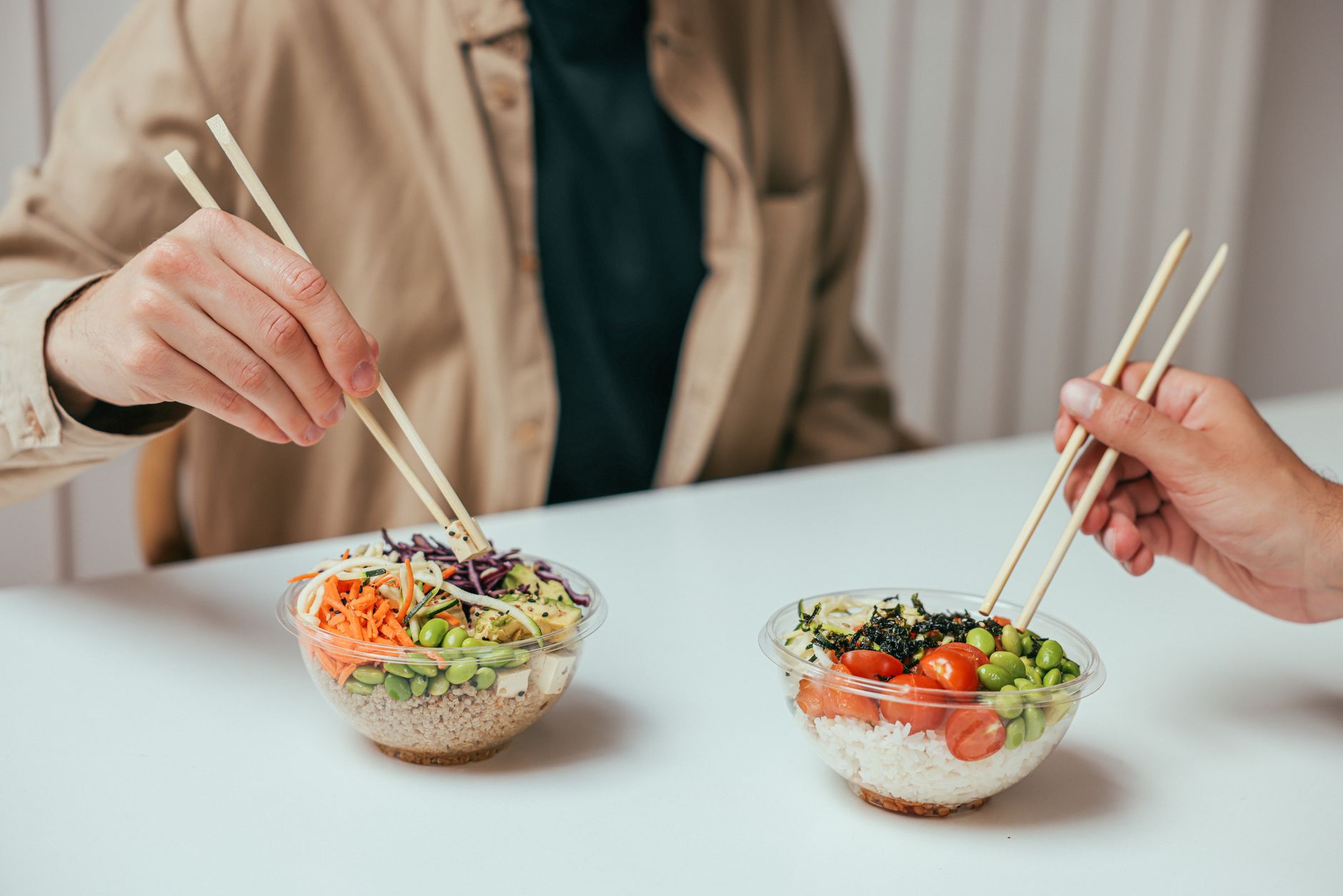 白い机をはさんで向かい合い、ごはんの入った器をはしで食べる2人の手元。