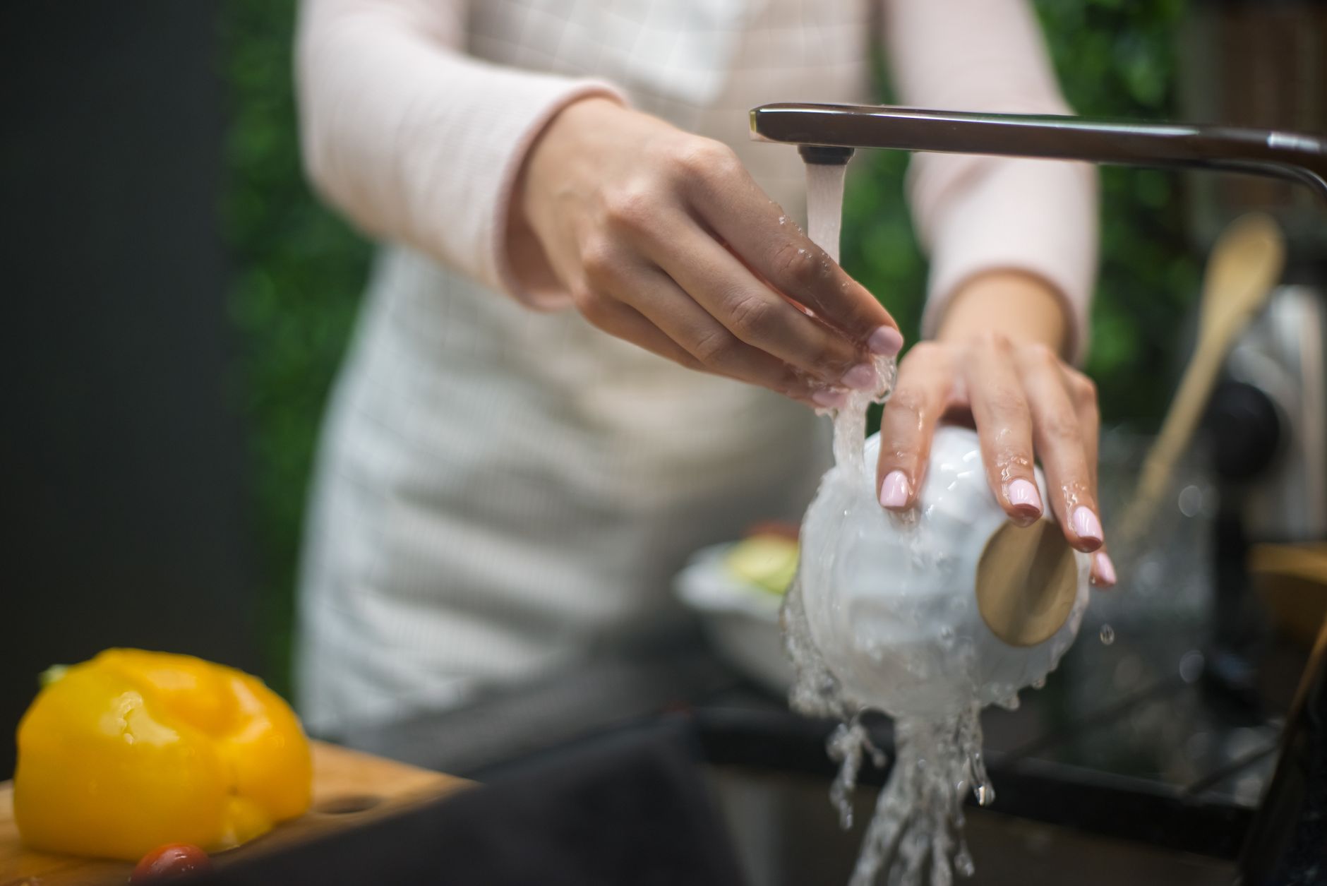 台所の流しで、蛇口の水を当てながら白い器を手で洗っているところ。