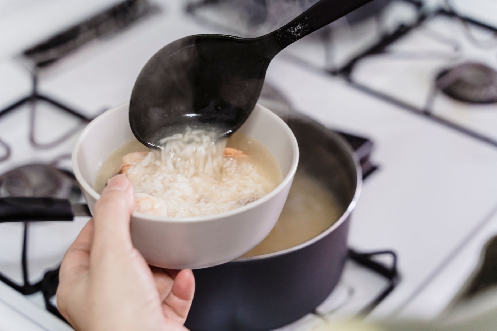 こんろのなべから、お玉ですくったごはんを白い器に移している手元。