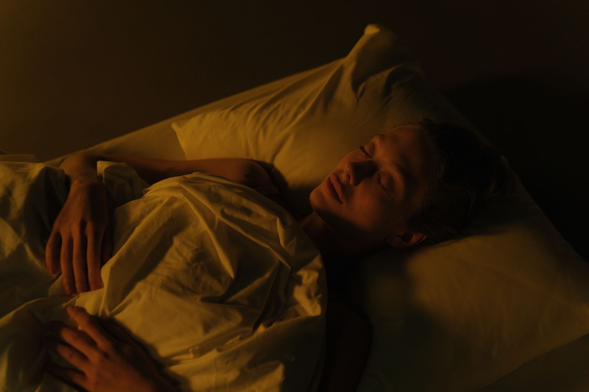 間接照明だけがともる夜の寝室で、白い掛け布団にくるまり眠っている人。