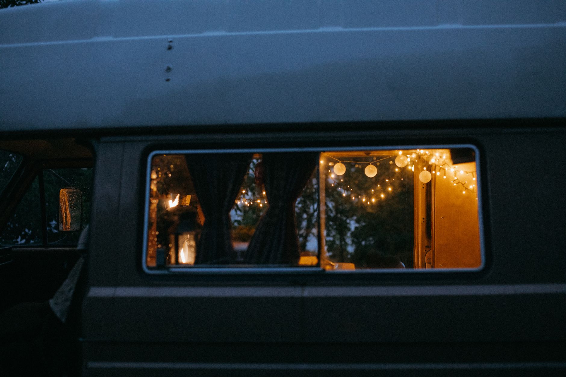 夕暮れの車の側面。少し開いた窓から、明かりのついた車内が見えている。